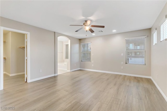 unfurnished bedroom featuring light wood finished floors, visible vents, arched walkways, baseboards, and a spacious closet