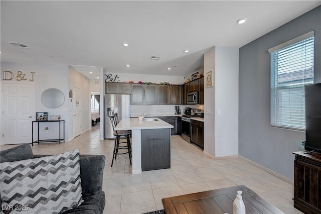 kitchen with light tile patterned floors, stainless steel appliances, a sink, dark brown cabinets, and light countertops