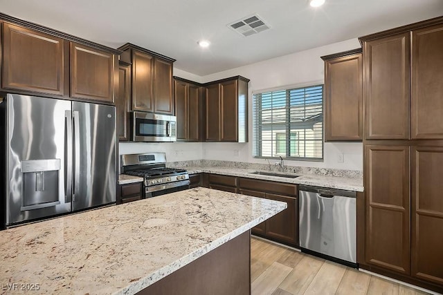 kitchen featuring dark brown cabinetry, visible vents, light stone countertops, stainless steel appliances, and a sink