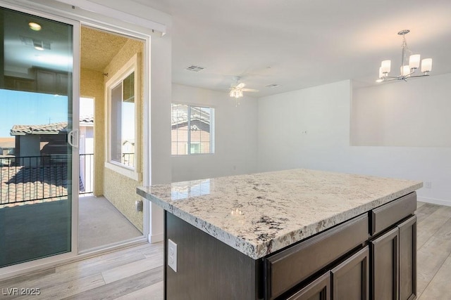 kitchen with light stone counters, light wood-style flooring, ceiling fan with notable chandelier, visible vents, and a center island