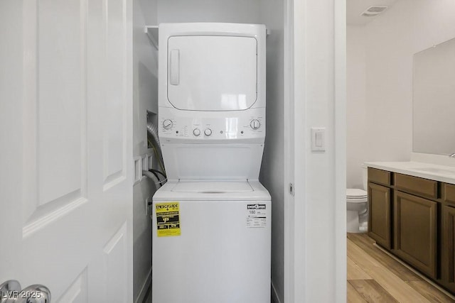 laundry room featuring light wood-style floors, stacked washer / dryer, laundry area, and a sink