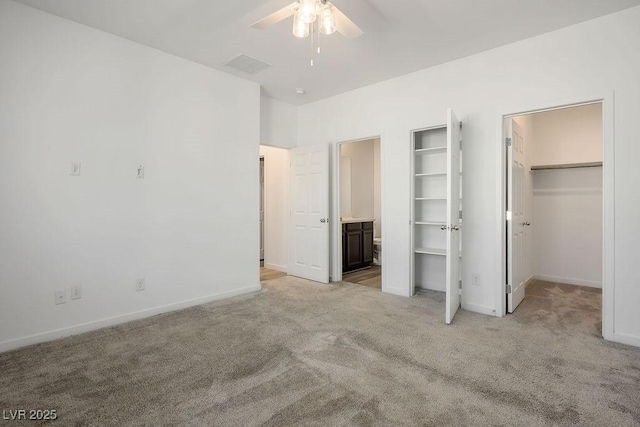 unfurnished bedroom featuring a walk in closet, light colored carpet, visible vents, ensuite bath, and baseboards