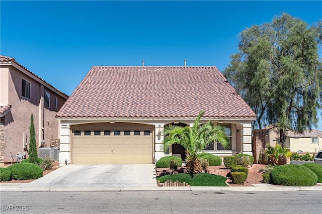 mediterranean / spanish home featuring an attached garage, central air condition unit, a tile roof, concrete driveway, and stucco siding