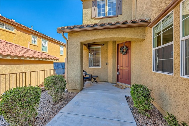 doorway to property with stucco siding, a tile roof, and fence