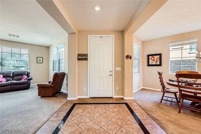 foyer entrance featuring light colored carpet, light tile patterned flooring, visible vents, and baseboards