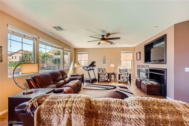 tiled living room featuring visible vents, a fireplace, baseboards, and a ceiling fan