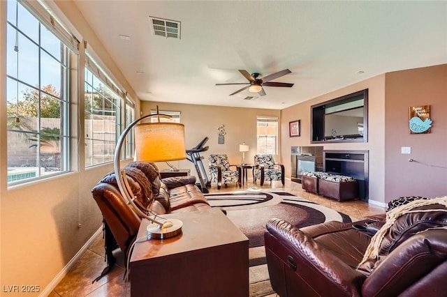 tiled living room featuring visible vents, baseboards, a glass covered fireplace, and a ceiling fan