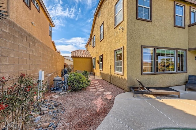 view of side of home featuring stucco siding, a patio area, a tile roof, and fence