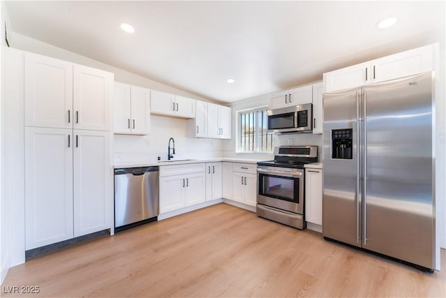 kitchen with light countertops, light wood-style flooring, appliances with stainless steel finishes, white cabinetry, and a sink