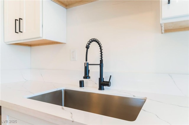 interior details with white cabinetry, light stone counters, and a sink