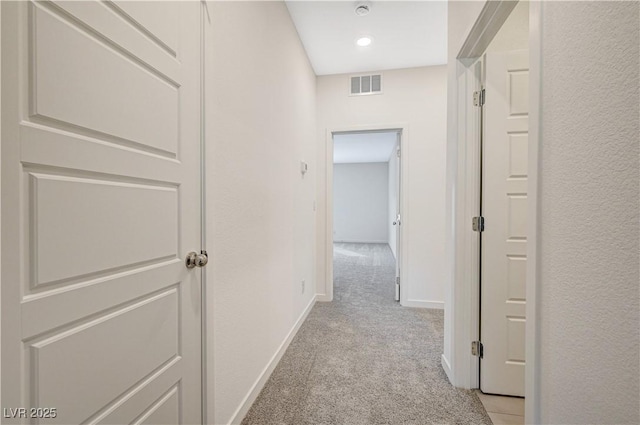 corridor featuring baseboards, visible vents, and light colored carpet