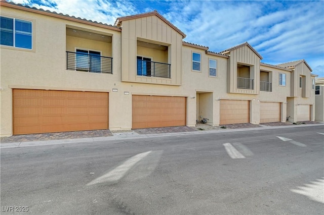 townhome / multi-family property with a garage, a tiled roof, board and batten siding, and stucco siding