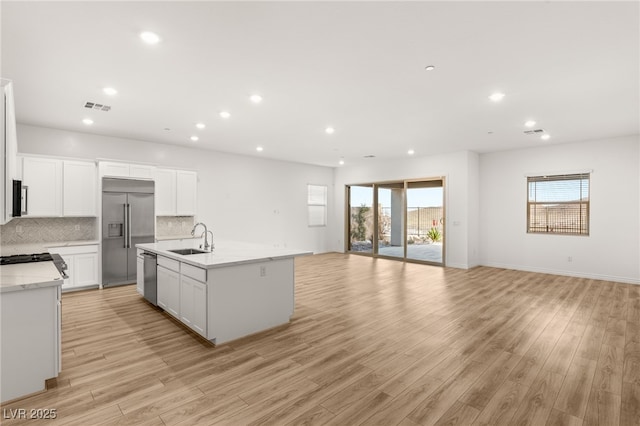 kitchen featuring stainless steel appliances, visible vents, decorative backsplash, open floor plan, and a sink