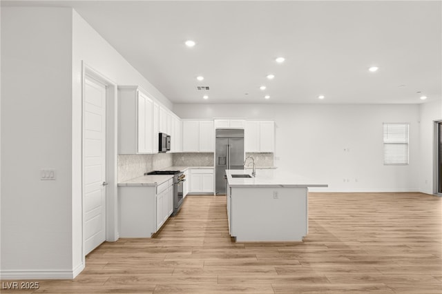 kitchen featuring visible vents, light wood-style flooring, a kitchen island with sink, a sink, and high quality appliances