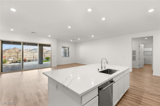 kitchen with white cabinets, open floor plan, stainless steel dishwasher, light wood-style floors, and a sink