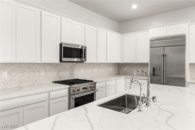 kitchen with a sink, white cabinetry, decorative backsplash, light stone countertops, and high end appliances