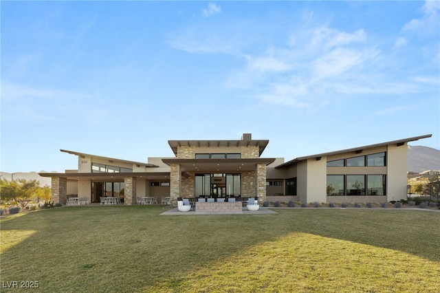 back of property with stone siding, a patio area, stucco siding, and a yard