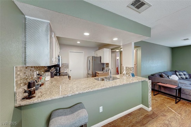 kitchen with stainless steel appliances, a peninsula, a sink, visible vents, and backsplash