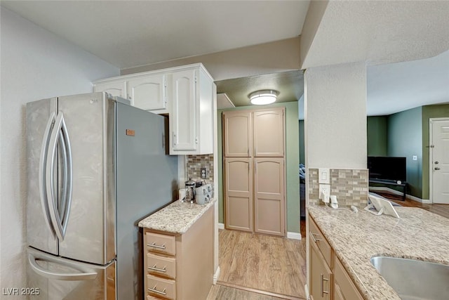 kitchen with light wood finished floors, light stone countertops, freestanding refrigerator, and tasteful backsplash