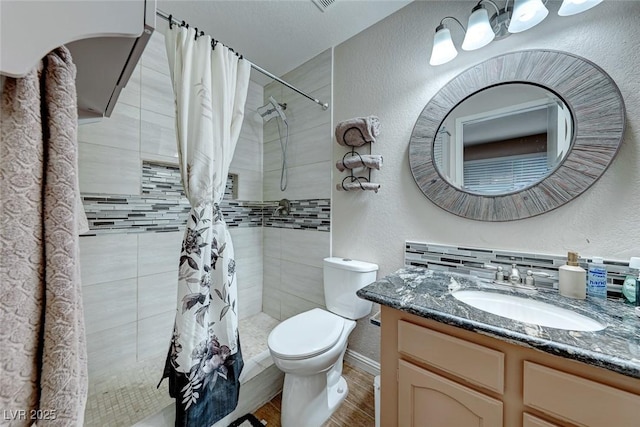 bathroom with tiled shower, a textured wall, vanity, and toilet