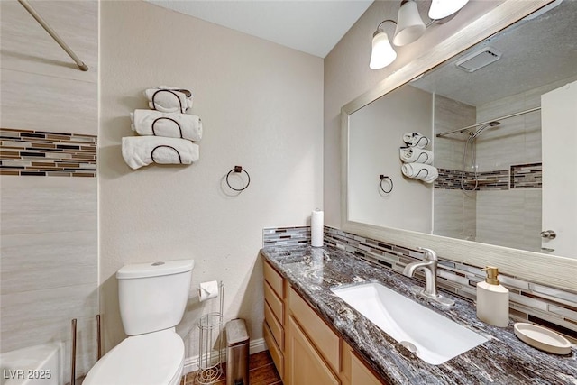 full bath with toilet, vanity, baseboards, tiled shower, and backsplash