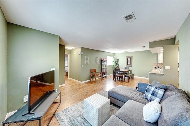 living area featuring baseboards, visible vents, and light wood finished floors