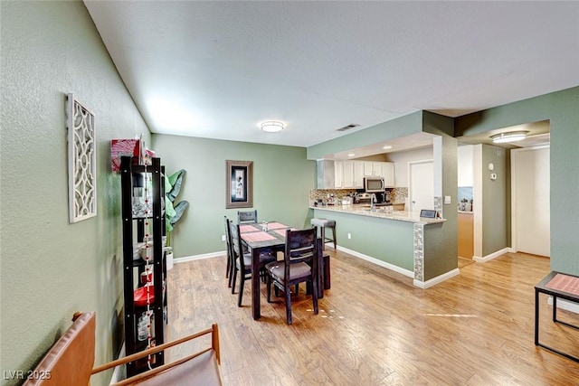 dining space with baseboards, visible vents, and light wood finished floors