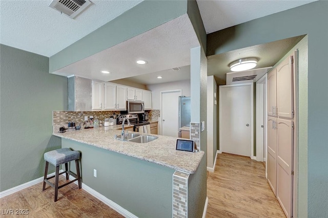 kitchen featuring light wood-style flooring, a peninsula, a sink, appliances with stainless steel finishes, and tasteful backsplash