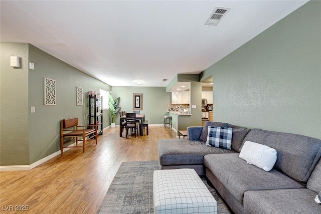 living room with light wood finished floors, visible vents, and baseboards