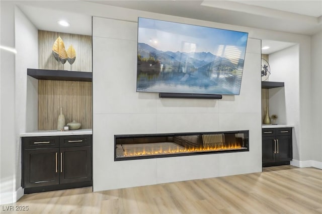 interior space featuring light wood finished floors, recessed lighting, baseboards, and a glass covered fireplace