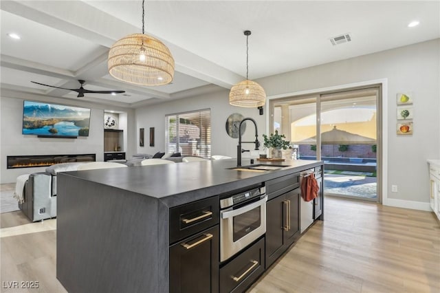 kitchen featuring visible vents, a glass covered fireplace, dark countertops, oven, and a sink