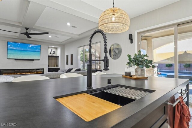 kitchen with coffered ceiling, a glass covered fireplace, a sink, beam ceiling, and recessed lighting