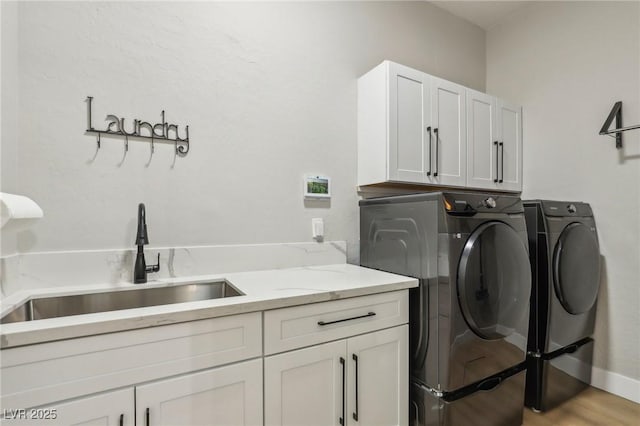 laundry area with cabinet space, light wood finished floors, a sink, and independent washer and dryer