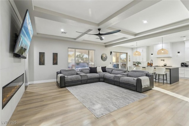 living area with a large fireplace, coffered ceiling, baseboards, light wood finished floors, and beamed ceiling