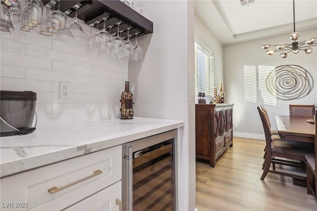 kitchen featuring light wood-style flooring, beverage cooler, white cabinetry, light stone countertops, and an inviting chandelier