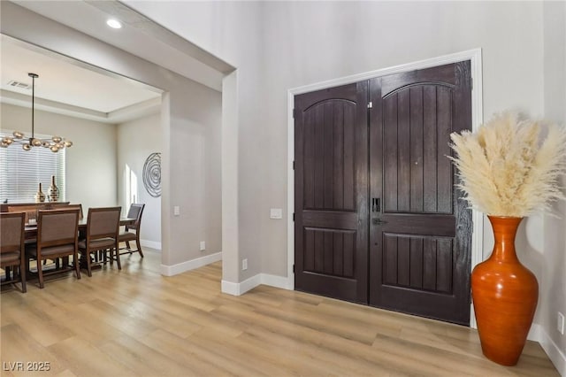 foyer entrance featuring light wood-type flooring, baseboards, visible vents, and a chandelier