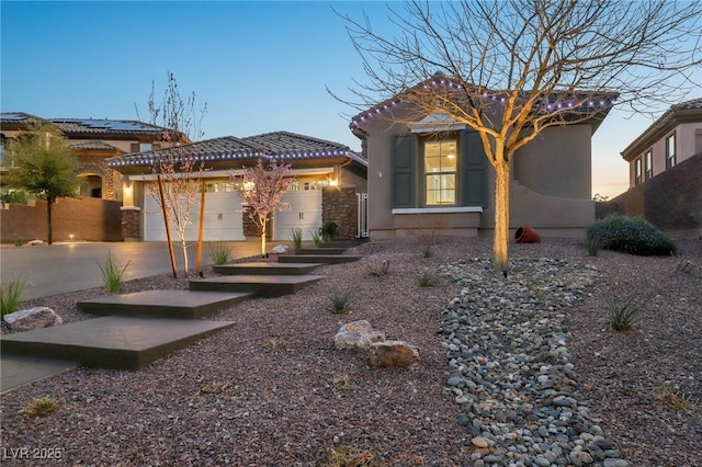 back of property at dusk featuring an attached garage, driveway, a tile roof, and stucco siding