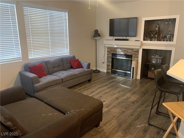 living area featuring a stone fireplace, baseboards, and wood finished floors