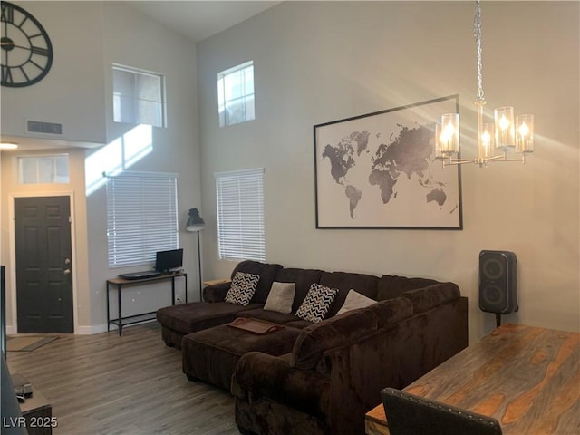 living room featuring wood finished floors, visible vents, a towering ceiling, and a chandelier