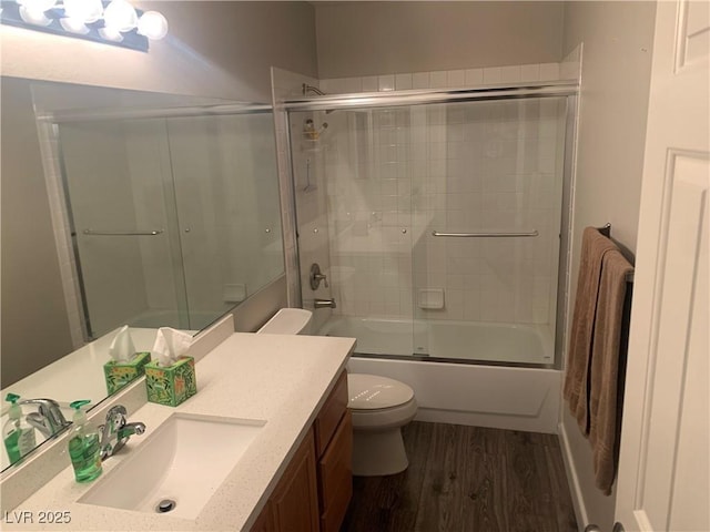 bathroom featuring shower / bath combination with glass door, toilet, wood finished floors, and vanity