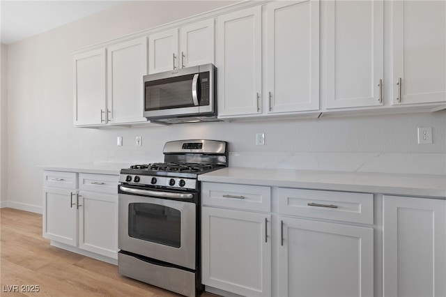 kitchen with light stone counters, stainless steel appliances, light wood-style flooring, white cabinets, and baseboards