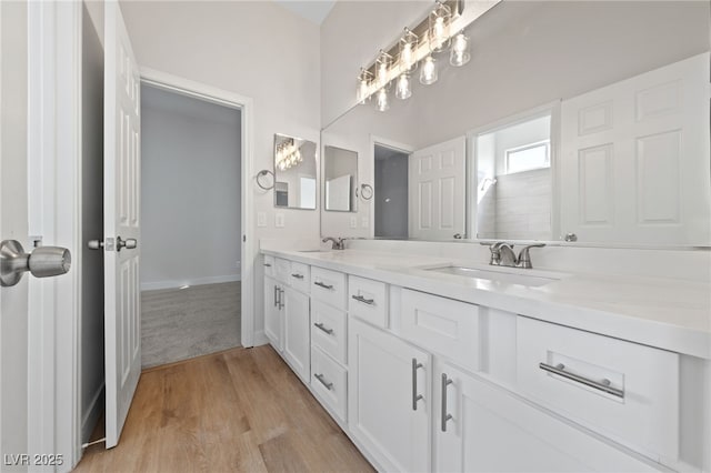 full bathroom featuring double vanity, wood finished floors, a sink, and baseboards