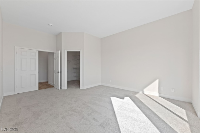 unfurnished bedroom with baseboards, a spacious closet, a closet, and light colored carpet