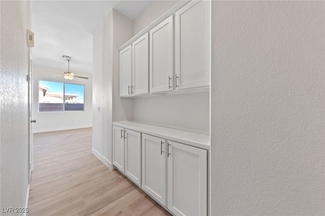 corridor featuring baseboards, a textured wall, and light wood-style floors