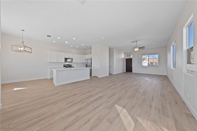 unfurnished living room featuring light wood-type flooring, baseboards, visible vents, and ceiling fan with notable chandelier