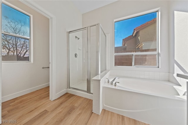 full bath featuring a stall shower, plenty of natural light, a garden tub, and wood finished floors