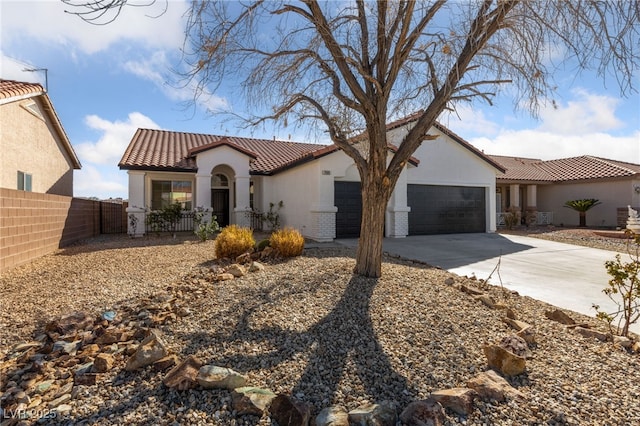 mediterranean / spanish-style home with a tile roof, stucco siding, concrete driveway, an attached garage, and fence