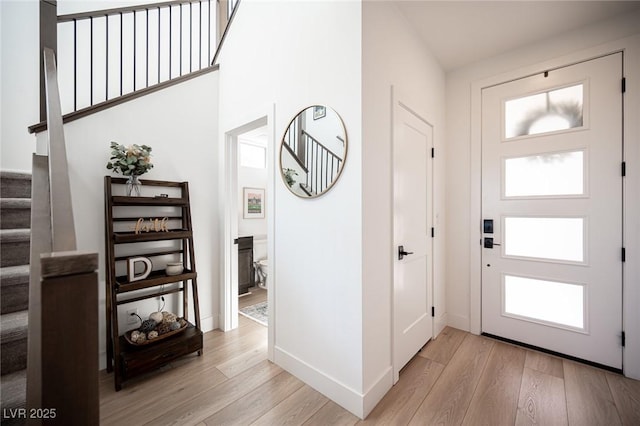 entryway with light wood-style floors, baseboards, and stairs