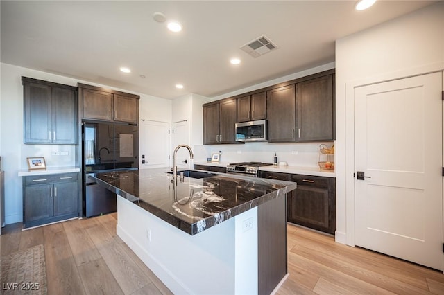 kitchen featuring appliances with stainless steel finishes, a sink, light wood finished floors, and dark brown cabinets