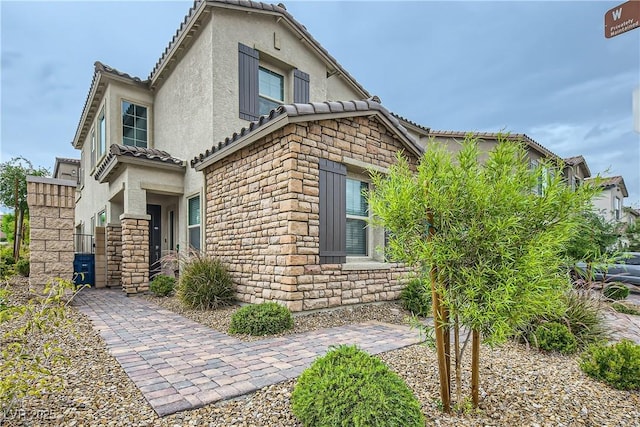 view of side of property featuring stone siding, a tile roof, and stucco siding